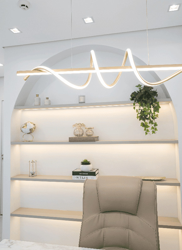 Detalhe da recepção do consultório com nicho em arco iluminado, prateleiras com objetos decorativos, planta pendente e luminária de LED contínua dourada, fotografia de interiores ultra-realista